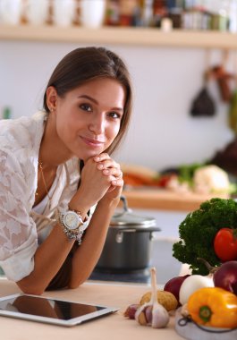 Mutfakta yemek yapmak için tablet bilgisayar kullanan genç bir kadın.