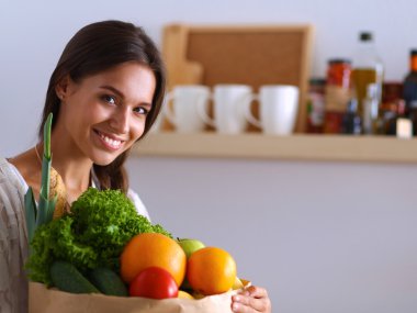 Elinde sebzeli alışveriş torbası tutan genç bir kadın. 