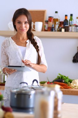 Mutfakta yemek yapmak için tablet bilgisayar kullanan genç bir kadın.
