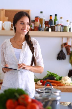 Mutfakta yemek yapmak için tablet bilgisayar kullanan genç bir kadın.