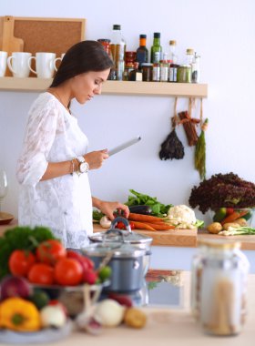 Mutfakta yemek yapmak için tablet bilgisayar kullanan genç bir kadın.