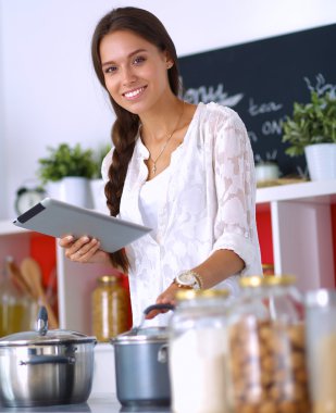 Mutfakta yemek yapmak için tablet bilgisayar kullanan genç bir kadın.