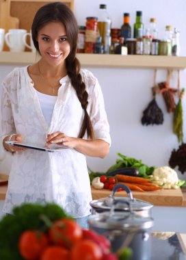 Mutfakta yemek yapmak için tablet bilgisayar kullanan genç bir kadın.