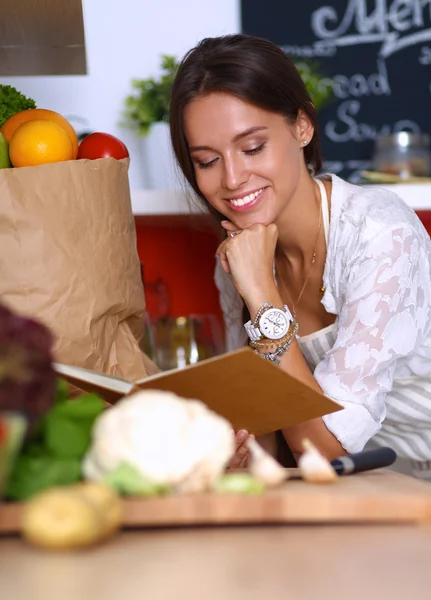 Ung kvinna läser kokbok i köket, letar efter recept — Stockfoto