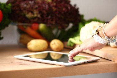 Mutfakta yemek yapmak için tablet bilgisayar kullanan genç bir kadın.