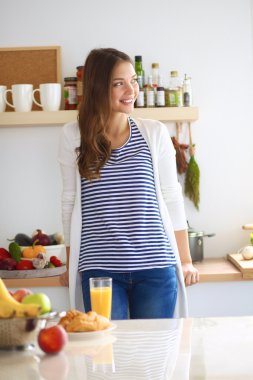 Mutfakta elinde meyve suyu ve kekle bekleyen genç bir kadın.