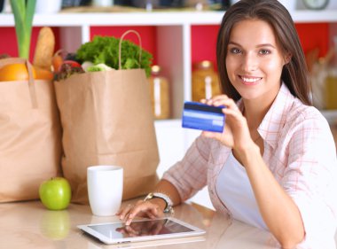 Gülümseyen kadın mutfakta tablet ve kredi kartı kullanarak alışveriş online