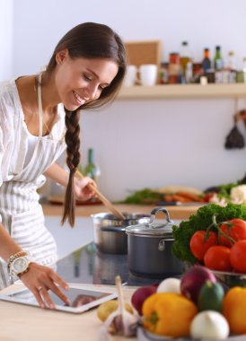 Mutfakta yemek yapmak için tablet bilgisayar kullanan genç bir kadın.