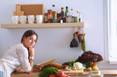 Mutfakta yemek kitabı okuyan genç bir kadın yemek tarifi arıyor.