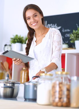 Mutfakta yemek yapmak için tablet bilgisayar kullanan genç bir kadın.