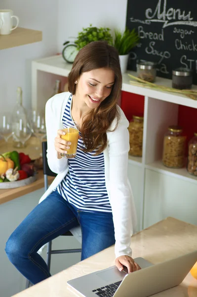 Dizüstü bilgisayar kullanarak ve mutfakta oturmuş çekici genç kadın 