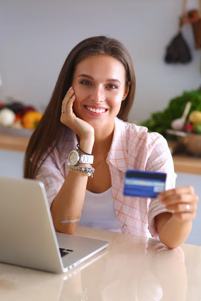 Mujer sonriente compras en línea utilizando la tableta y la tarjeta de crédito en la cocina —  Fotos de Stock