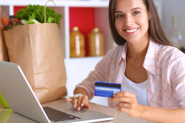 Mulher sorrindo compras on-line usando tablet e cartão de crédito na cozinha — Fotografia de Stock