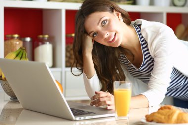 Dizüstü bilgisayar kullanarak ve mutfakta oturmuş çekici genç kadın 