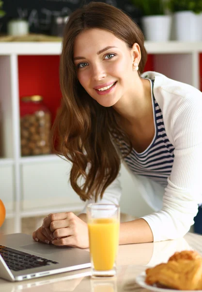 Mujer joven atractiva usando el ordenador portátil y sentado en la cocina —  Fotos de Stock