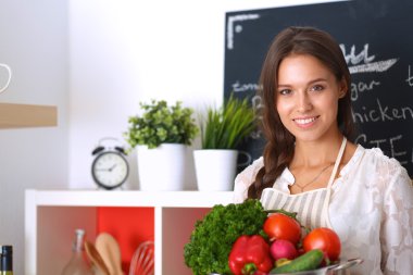Mutfakta elinde sebzelerle gülümseyen genç bir kadın.