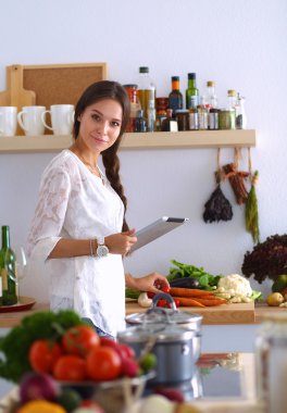 Mutfakta yemek yapmak için tablet bilgisayar kullanan genç bir kadın.