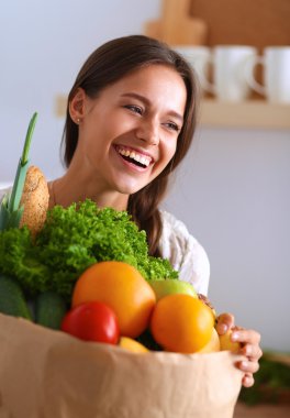 Elinde sebzeli alışveriş torbası tutan genç bir kadın. 