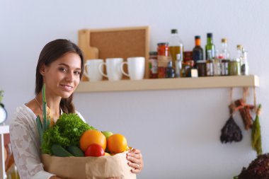 Elinde sebzeli alışveriş torbası tutan genç bir kadın. 