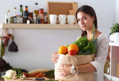 Elinde sebzeli alışveriş torbası tutan genç bir kadın. 