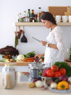 Mutfakta yemek yapmak için tablet bilgisayar kullanan genç bir kadın.