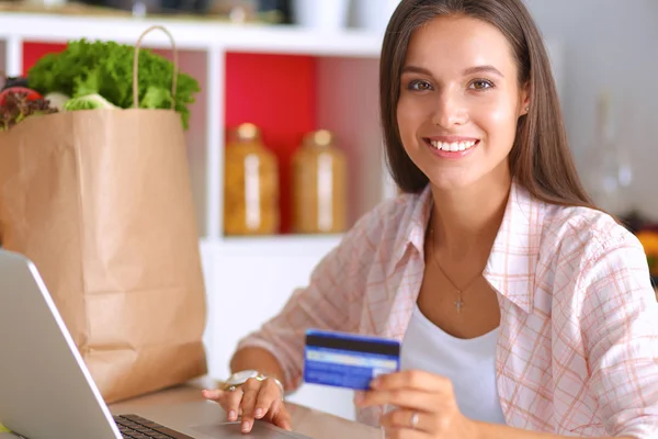 Lachende vrouw online winkelen met behulp van Tablet PC- en creditcard in keuken — Stockfoto