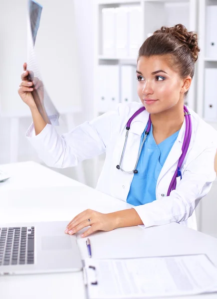 Doctora joven estudiando imagen de rayos X sentada en el escritorio —  Fotos de Stock