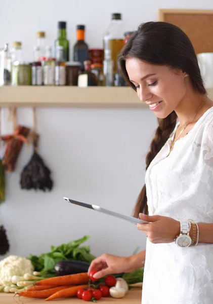 부엌에서 요리를 하기 위해 태블릿 컴퓨터를 사용하는 젊은 여자 — 스톡 사진