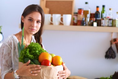 Elinde sebzeli alışveriş torbası tutan genç bir kadın. 