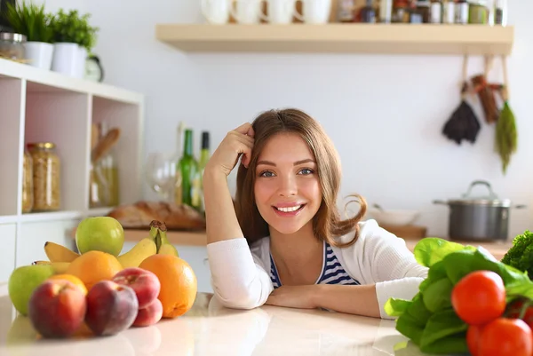 Mujer joven de pie cerca de escritorio en la cocina — Foto de Stock