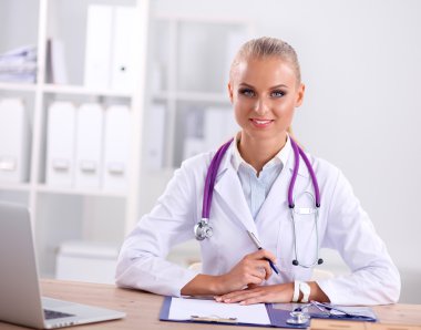 Güzel, genç, gülümseyen bayan doktor masada oturuyor ve yazıyor..