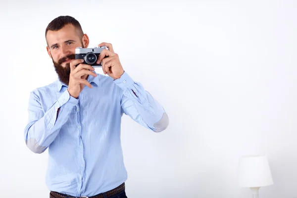 Joven barba hombre sosteniendo una cámara mientras está de pie sobre fondo blanco — Foto de Stock