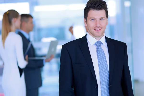 Portrait of young businessman in office with colleagues in the background — Stock Photo, Image