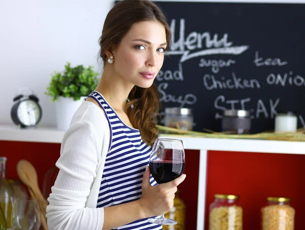 Mujer bonita bebiendo un poco de vino en casa en la cocina —  Fotos de Stock