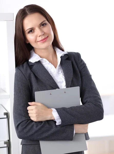 Attractive young businesswoman standing near desk with folder in the office — Stock Photo, Image