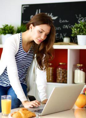 Dizüstü bilgisayar kullanarak ve mutfakta oturmuş çekici genç kadın 