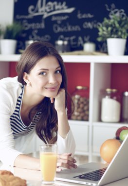 Dizüstü bilgisayar kullanarak ve mutfakta oturmuş çekici genç kadın 