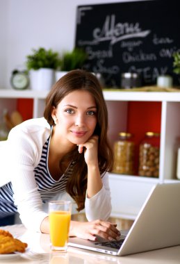 Dizüstü bilgisayar kullanarak ve mutfakta oturmuş çekici genç kadın 