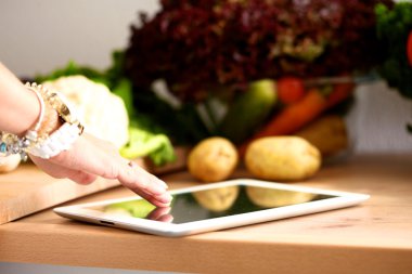 Mutfakta yemek yapmak için tablet bilgisayar kullanan genç bir kadın.