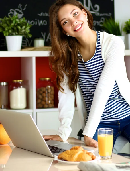 Attrayant jeune femme en utilisant un ordinateur portable et assis dans la cuisine — Photo