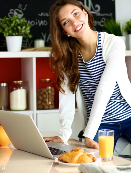 Attraente giovane donna che utilizza il computer portatile e seduto in cucina — Foto Stock