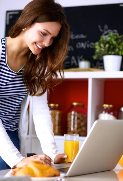 Attraktiv ung kvinna med laptop och sitter i köket — Stockfoto