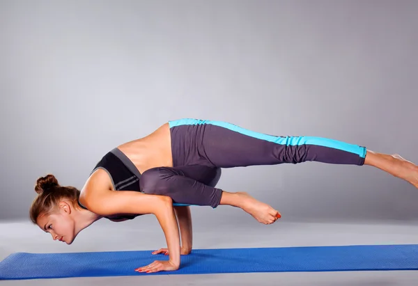 Mujer joven haciendo ejercicio de yoga sobre fondo gris — Foto de Stock