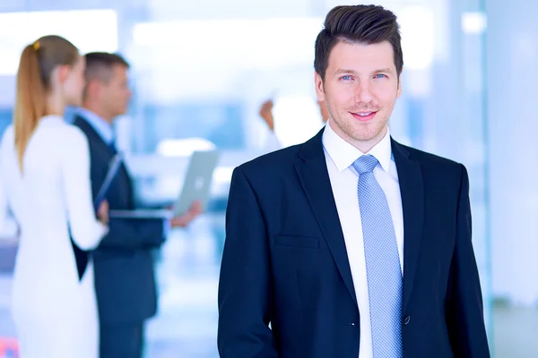 Portret van jonge zakenman in kantoor met collega's op de achtergrond — Stockfoto