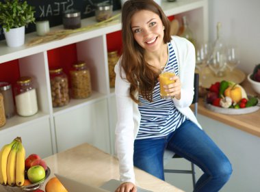 Dizüstü bilgisayar kullanarak ve mutfakta oturmuş çekici genç kadın