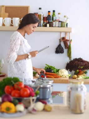 Mutfakta yemek yapmak için tablet bilgisayar kullanan genç bir kadın.