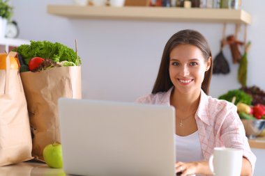 kahve fincanı ve dizüstü evde mutfakta gülümseyen genç kadın