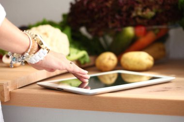 Mutfakta yemek yapmak için tablet bilgisayar kullanan genç bir kadın.