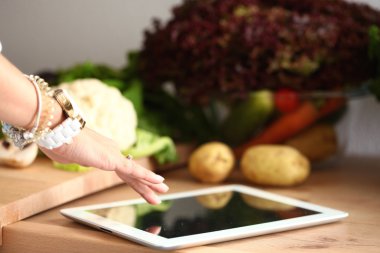 Mutfakta yemek yapmak için tablet bilgisayar kullanan genç bir kadın.