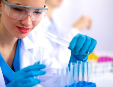 Kadın araştırmacı, beyaz arka planda izole edilmiş ilaç şişeleri ve mataralarla çevrili.